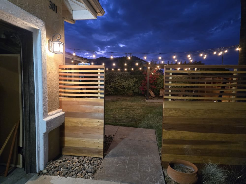 Horizontal wood fence with open lattice top and string lights over a patio